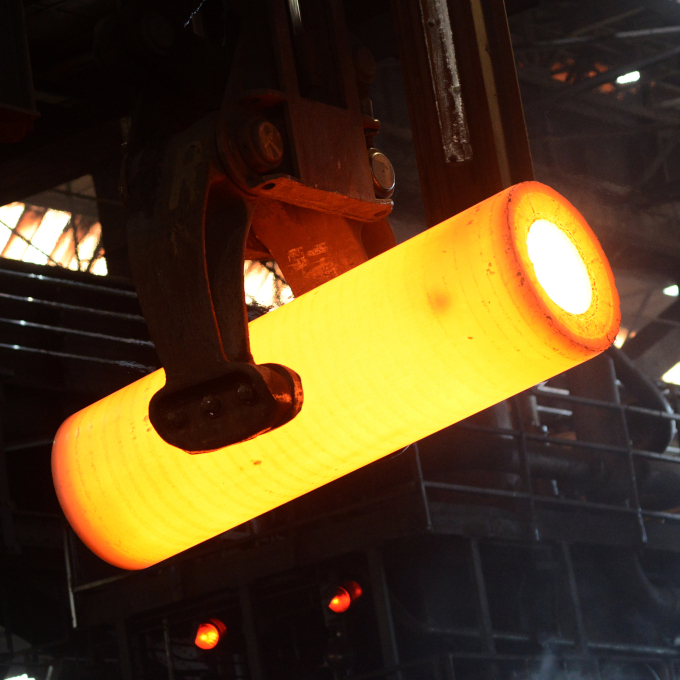 Ein glühendes Stahlrohr wird in der Produktion durch die Halle bewegt.