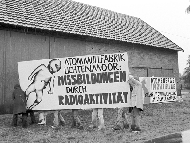 Demonstranten halten ein Plakat mit der Aufschrift: "Atommüllfabrik Lichtenmoor: Missbildungen durch Radioaktivität" (BildMitLangbeschreibung)